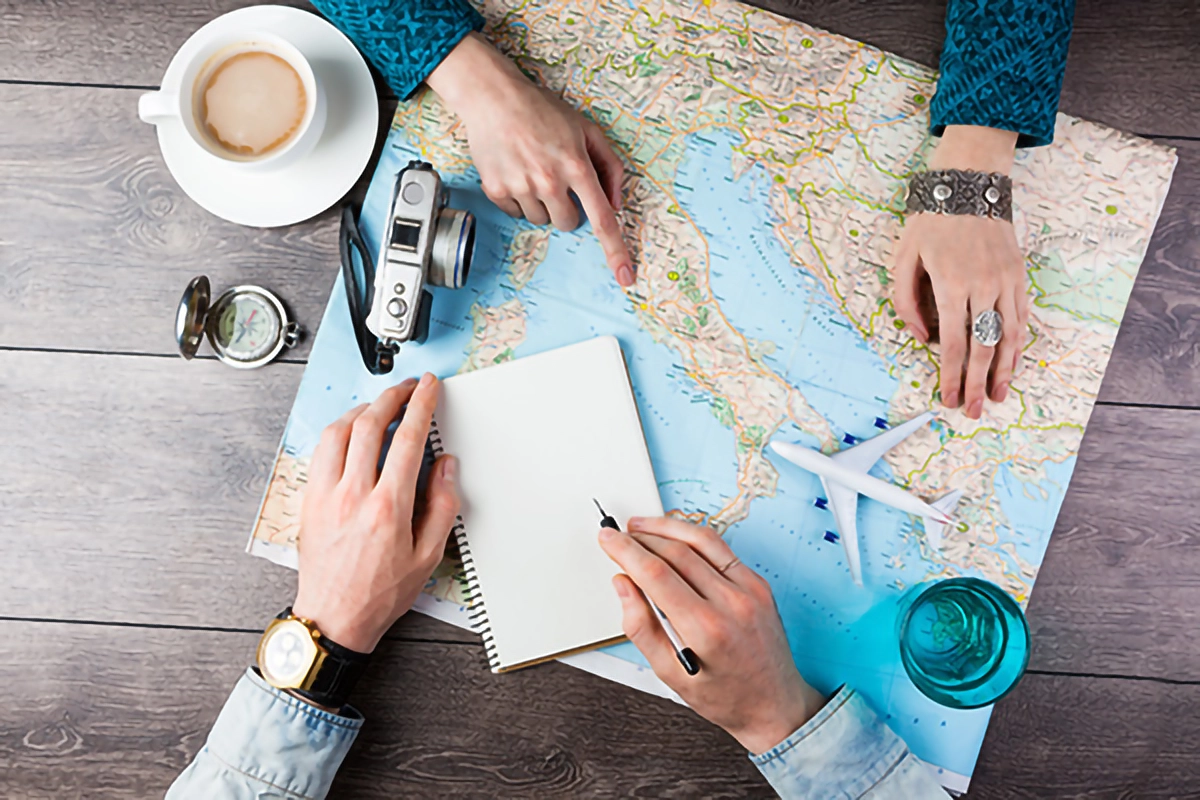 Image shows a world map on a tabel with drinks of tea and hands of travelers